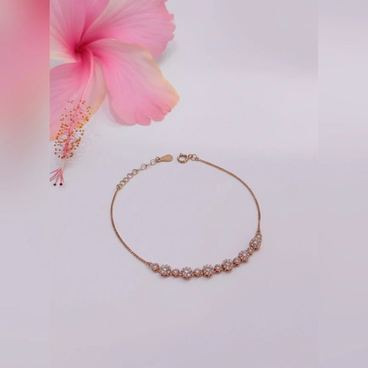 Gold bracelet on a light pink background with a pink flower