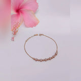 Gold bracelet on a light pink background with a pink flower
