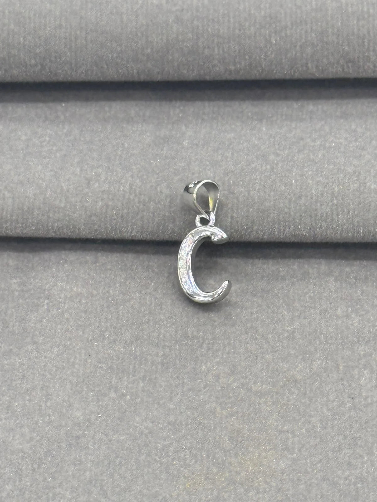 Silver C pendant on a gray fabric background