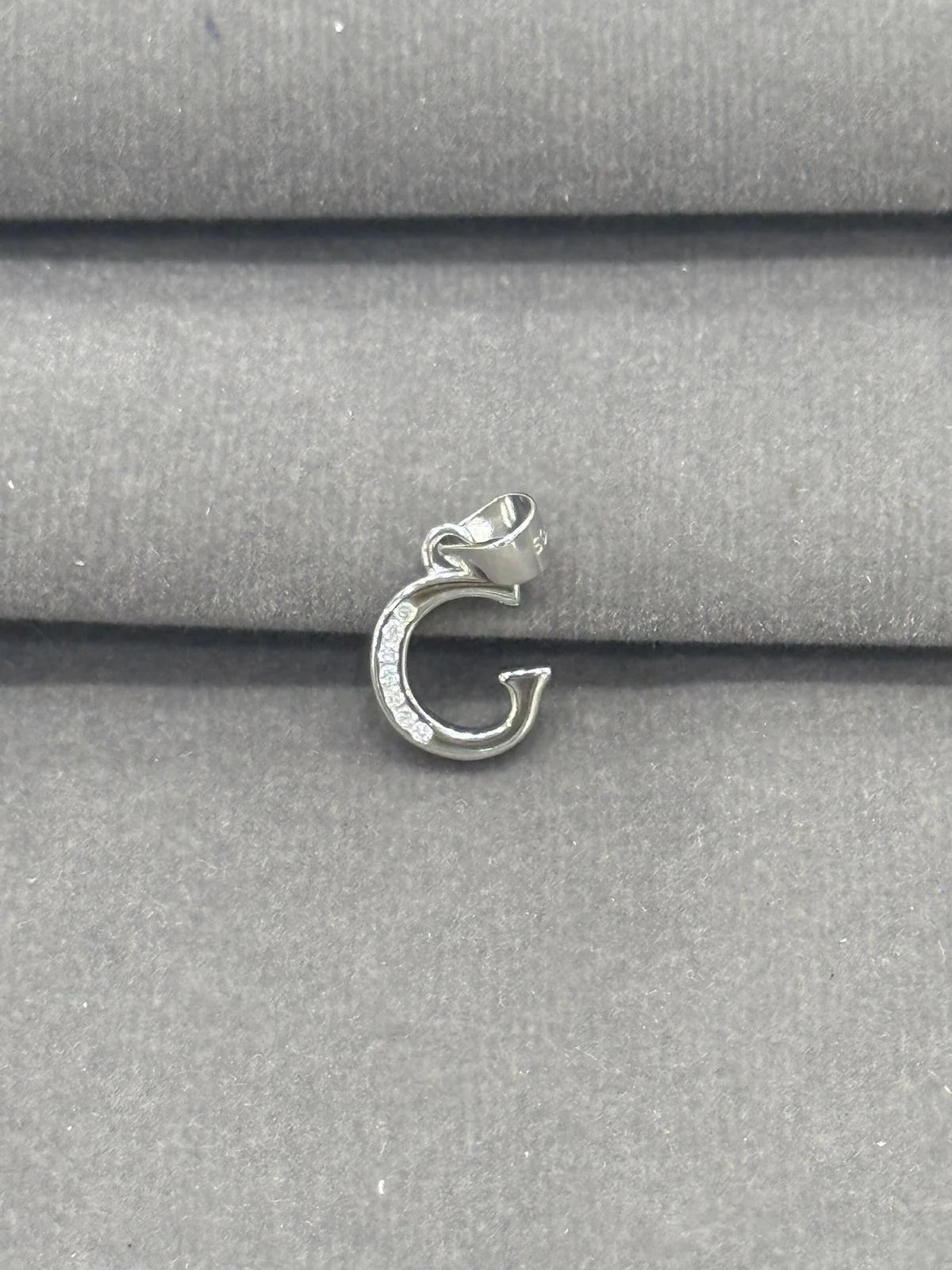 Silver pendant with a letter 'G' on a gray fabric background