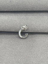 Silver pendant with a letter 'G' on a gray fabric background