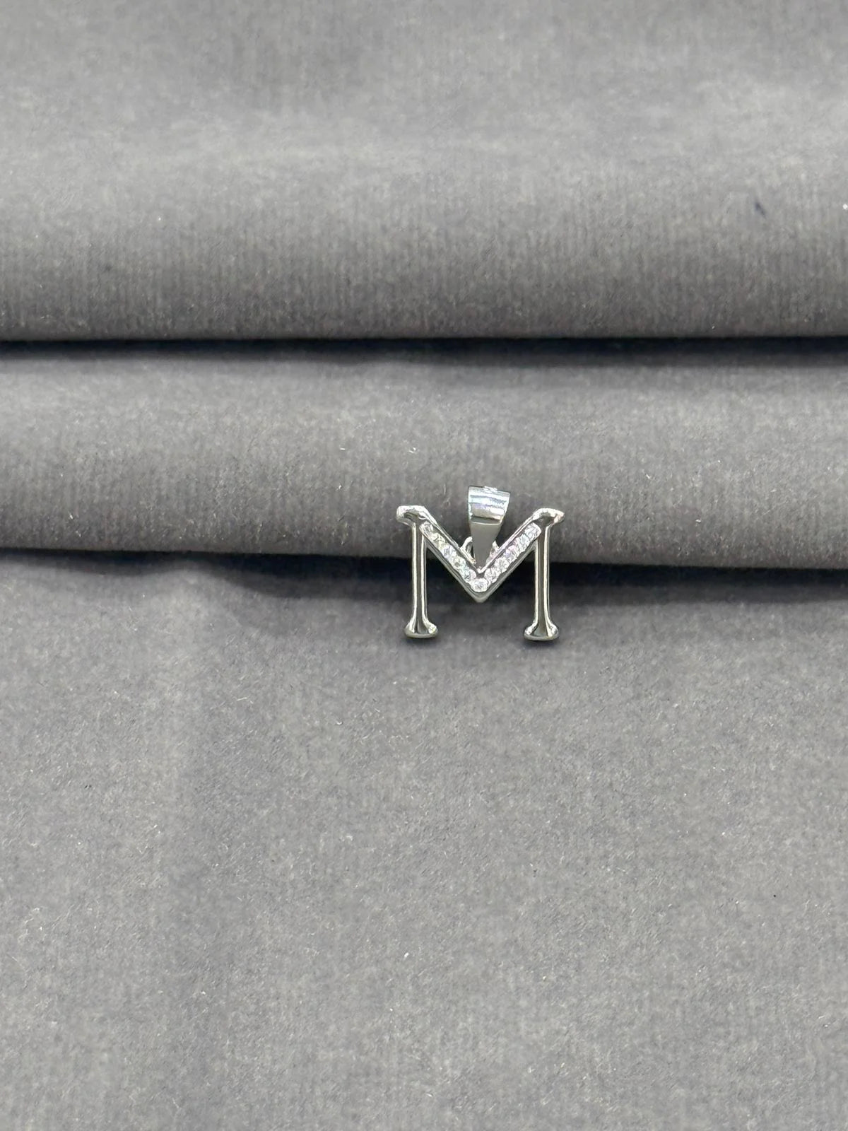 Silver letter 'M' earring on a gray fabric background