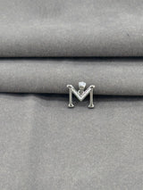 Silver letter 'M' earring on a gray fabric background
