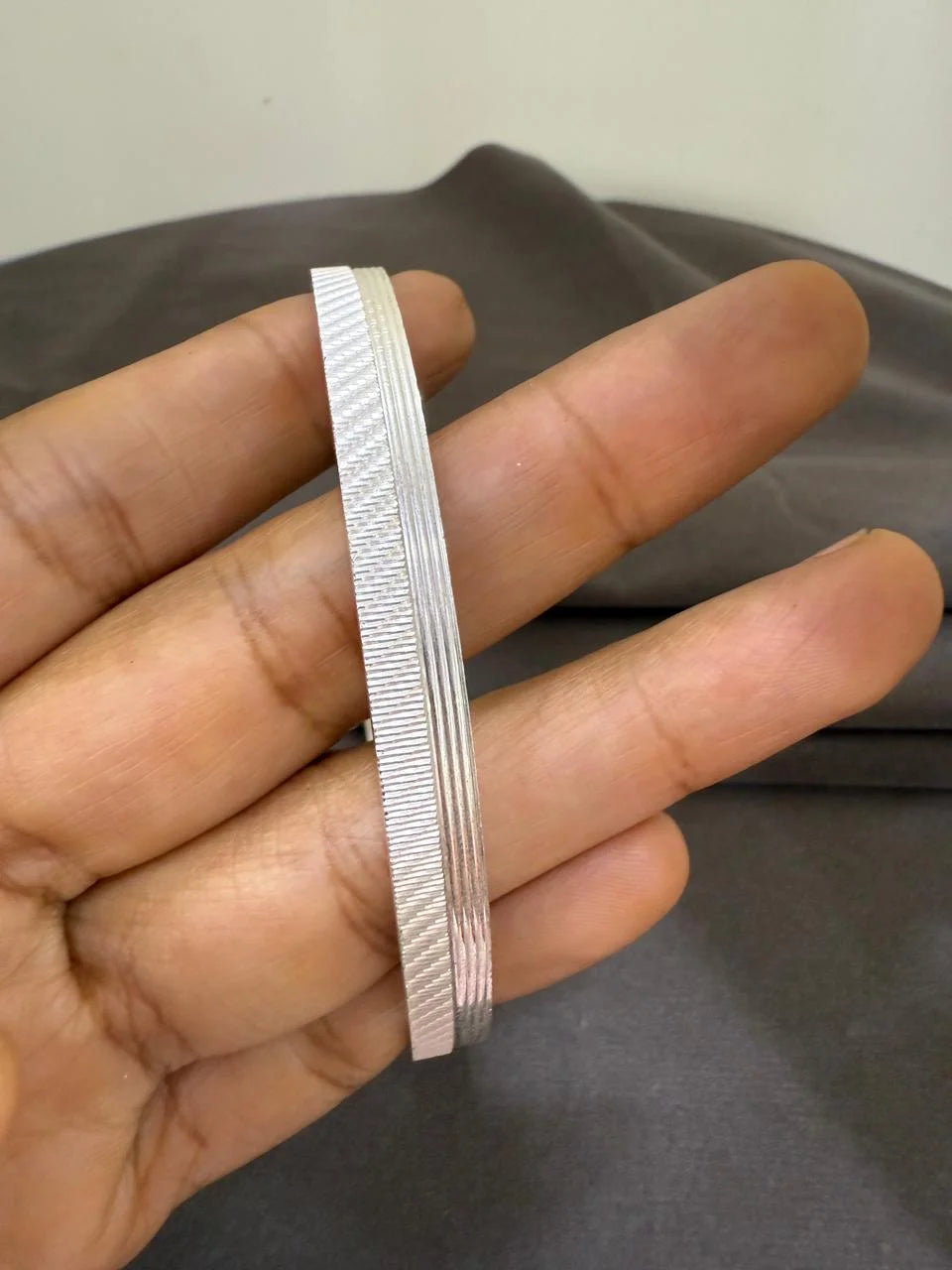 Silver bracelet held in a hand against a neutral background