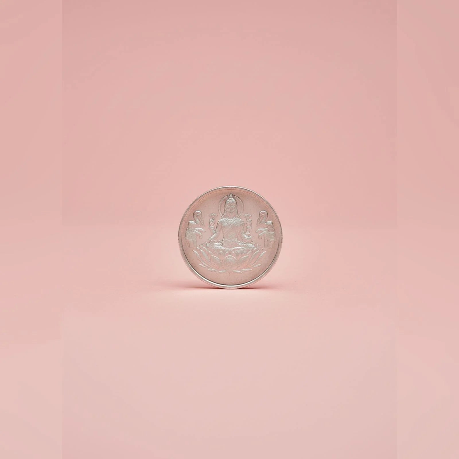 Silver coin with Lakshmifigure on a pink background