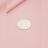 Silver coin with a design on a pink fabric background