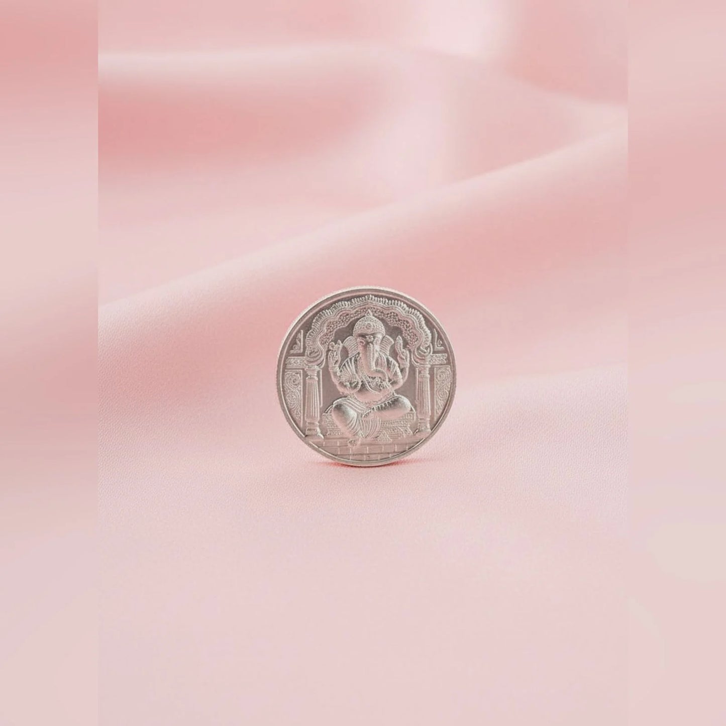 Silver coin with a deity figure on a pink and white gradient background