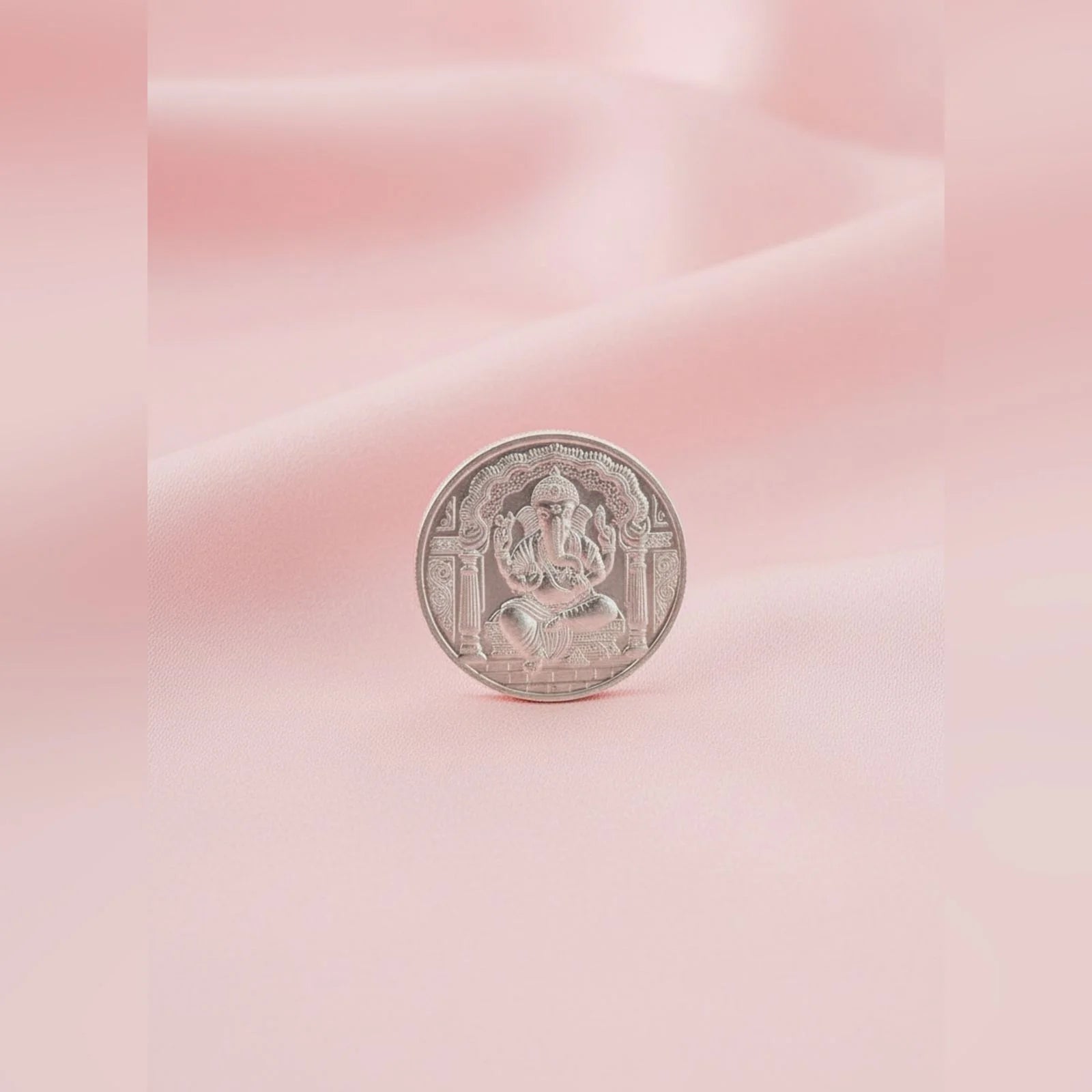 Silver coin with a deity figure on a pink and white gradient background