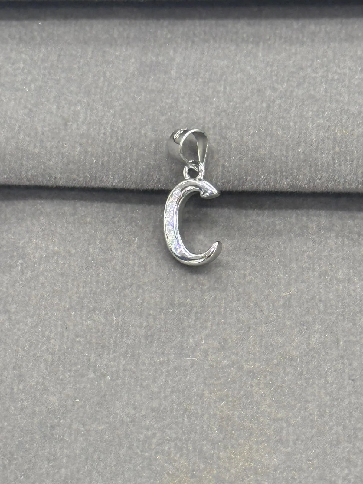 Silver C pendant on a gray fabric background