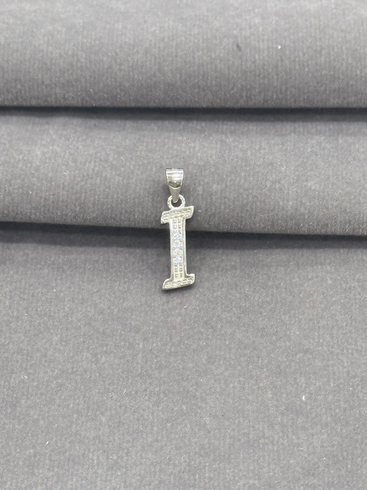 Silver letter 'I' pendant on a gray fabric background