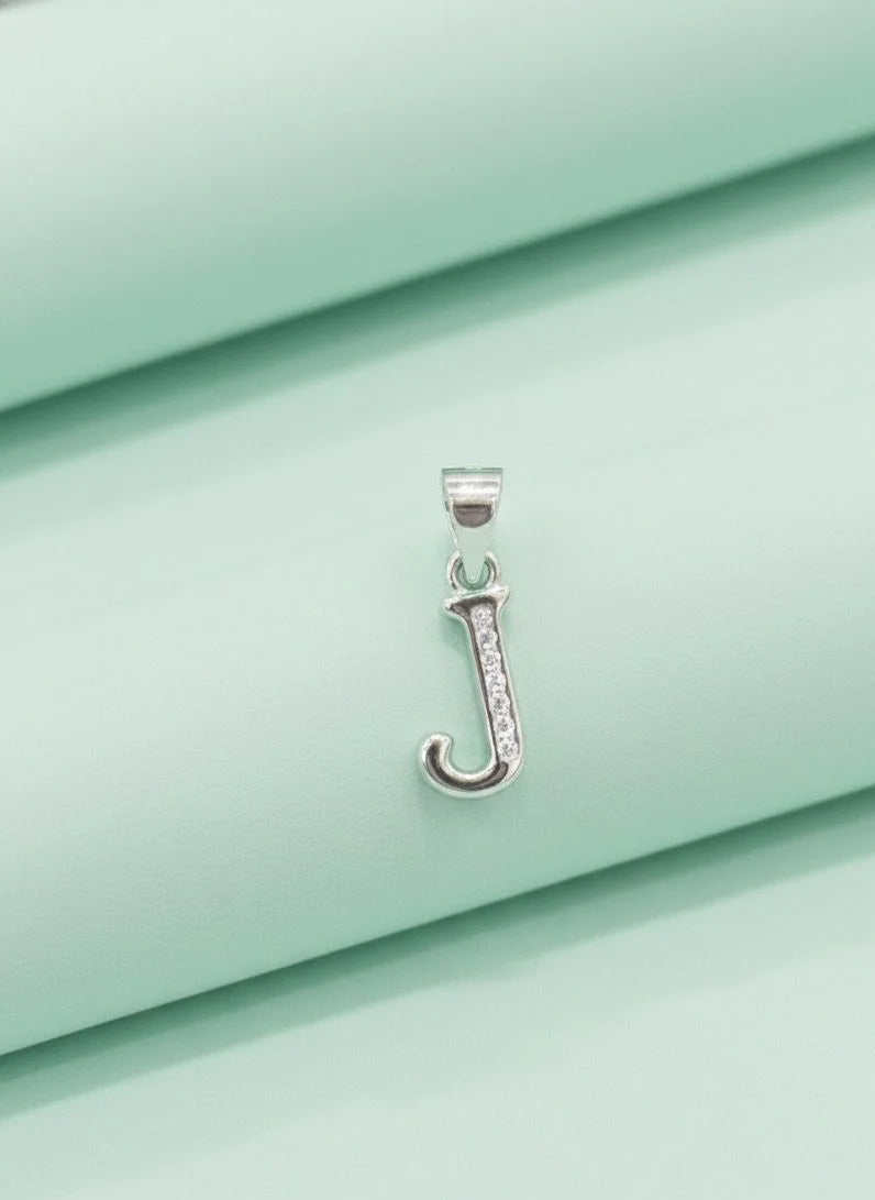 Silver pendant with a letter 'J' on a light green fabric background