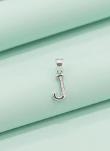 Silver pendant with a letter 'J' on a light green fabric background