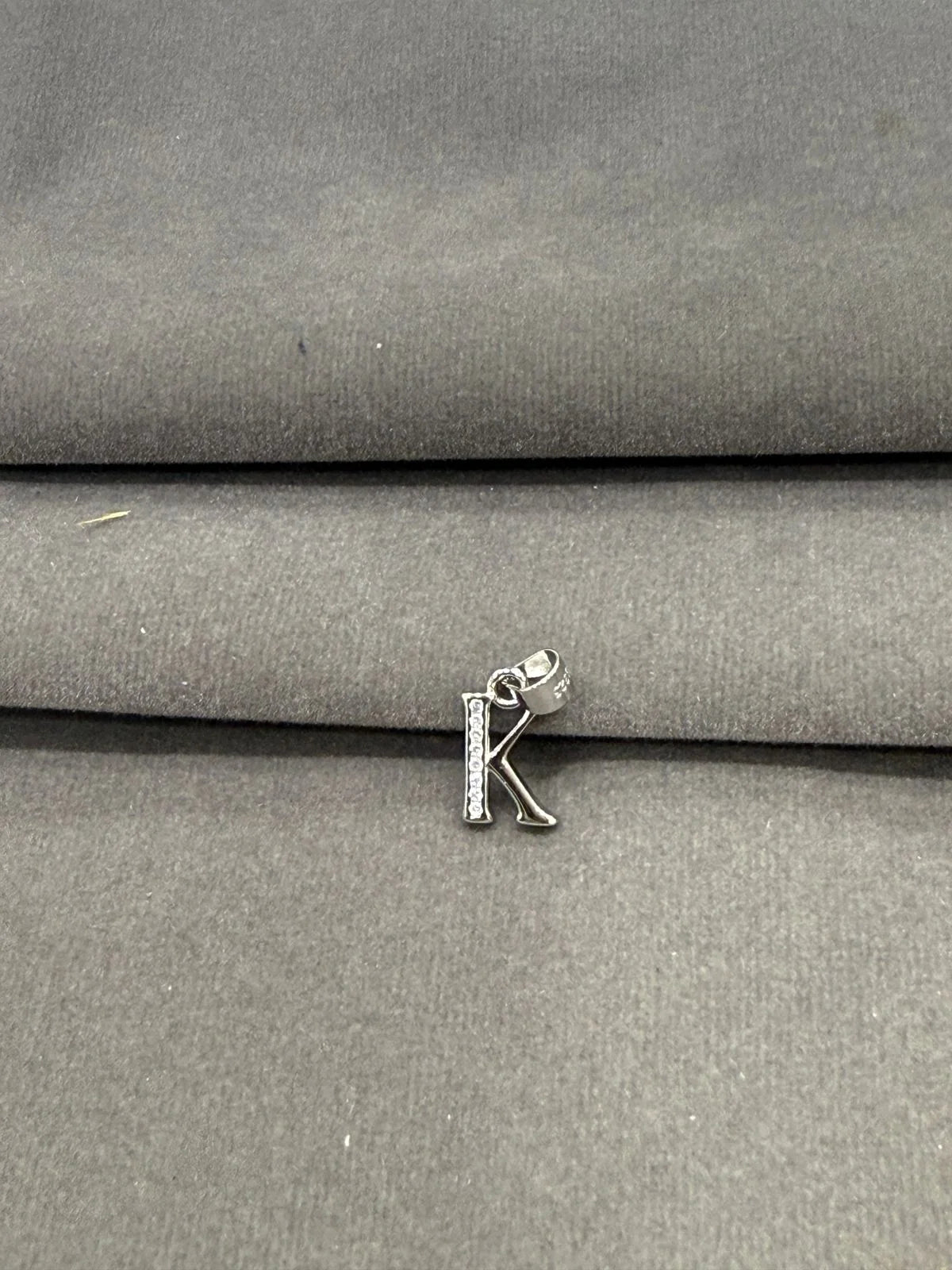 Silver letter 'K' charm on a gray fabric background