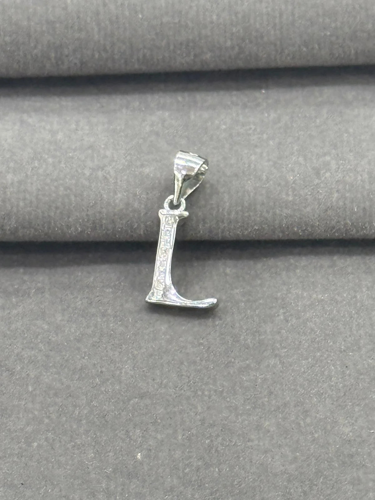 Silver 'L' pendant on a gray fabric background