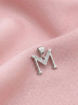 Silver letter 'M' pendant with clear stones on a pink fabric background