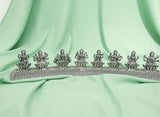 Decorative silver metal piece with figures on a light green fabric background