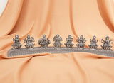 Silver deity statues on a decorative stand against an orange fabric background