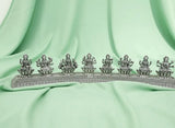 Decorative silver metal piece with figures on a light green fabric background