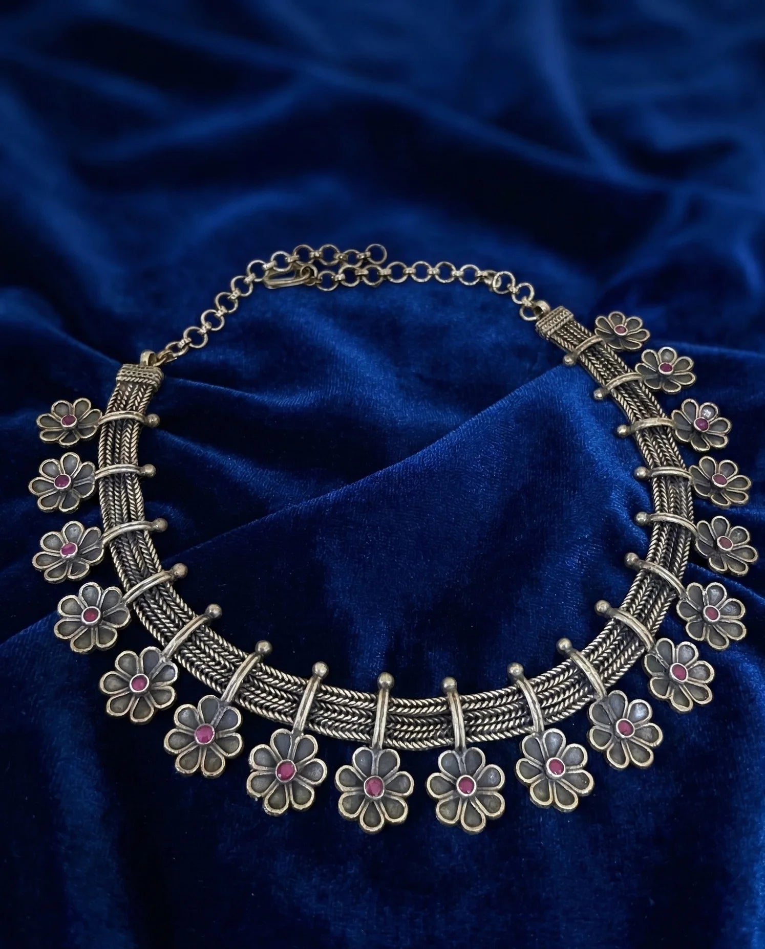 Decorative silver necklace with floral designs on a blue fabric background