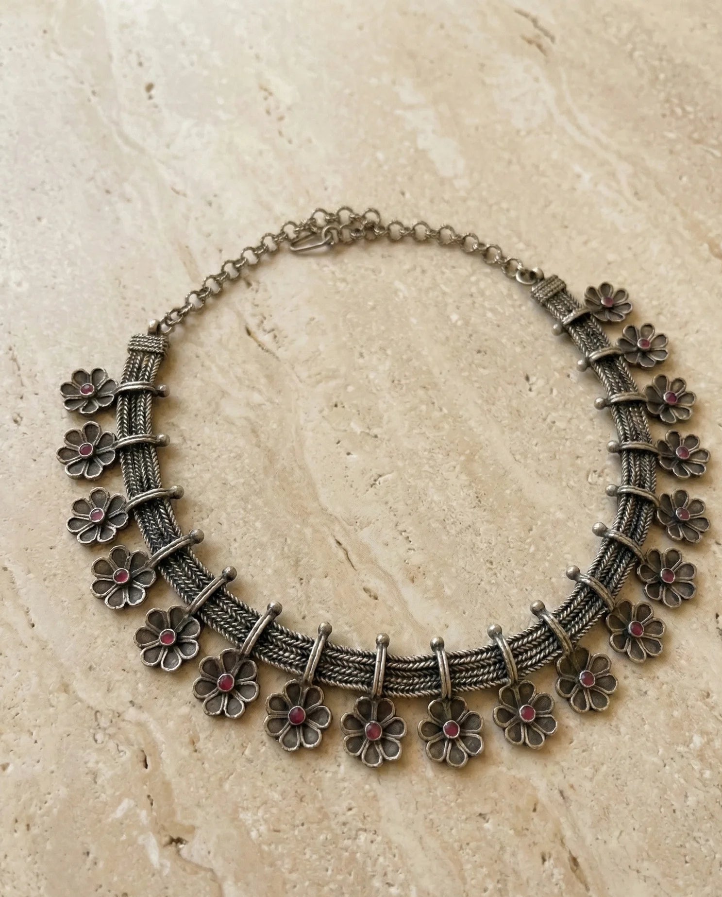 Silver floral necklace on a beige stone surface