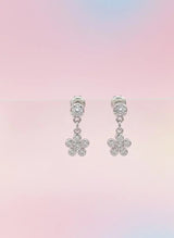Pair of silver flower-shaped earrings on a pastel gradient background