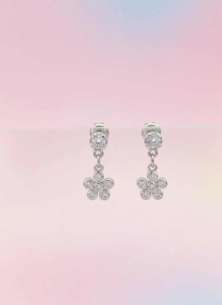Pair of silver flower-shaped earrings on a pastel gradient background