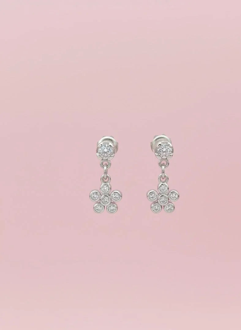 Pair of silver earrings with floral designs on a pink background