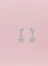 Pair of silver earrings with floral designs on a pink background