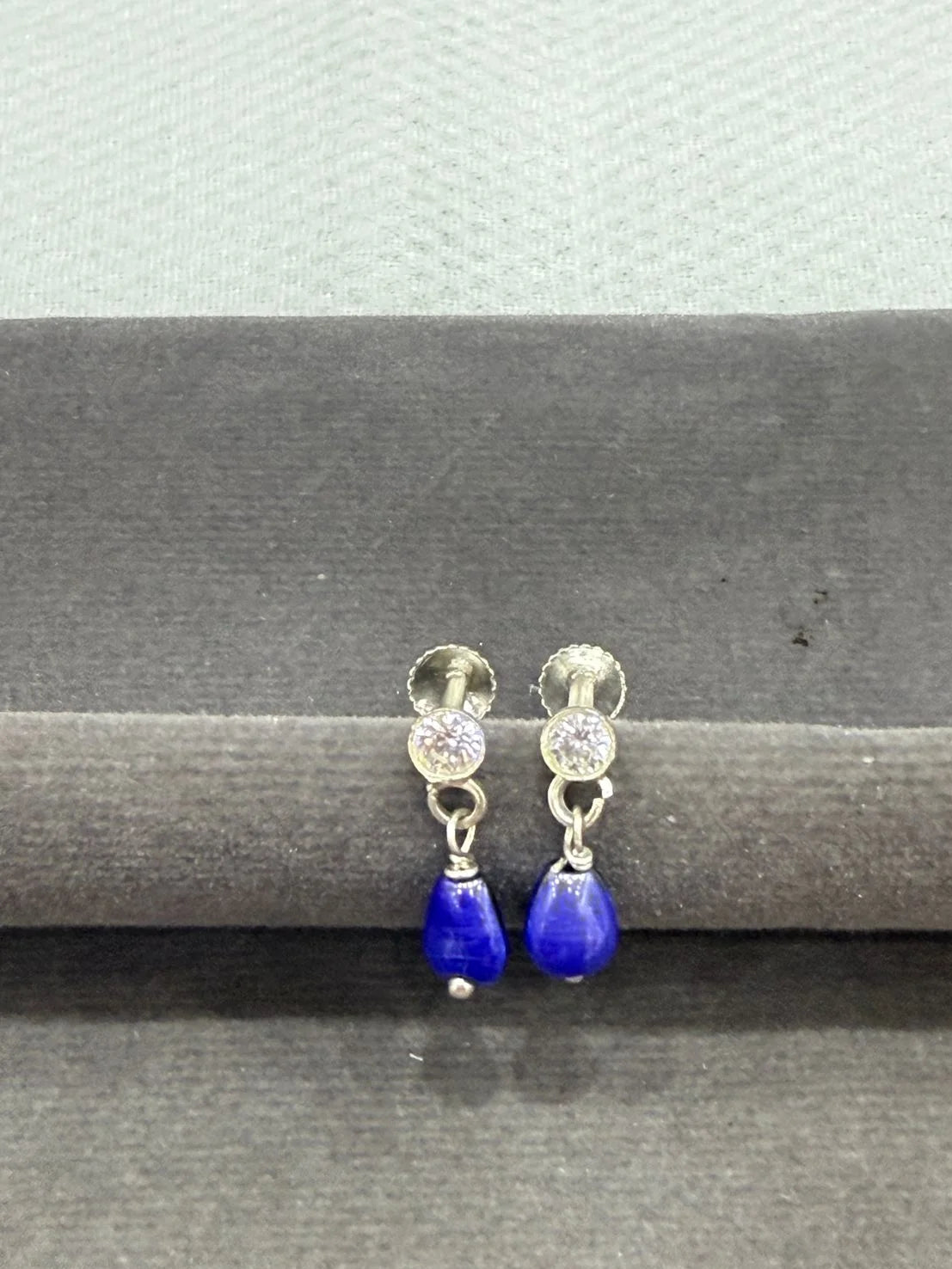 Pair of earrings with blue teardrop stones on a gray background