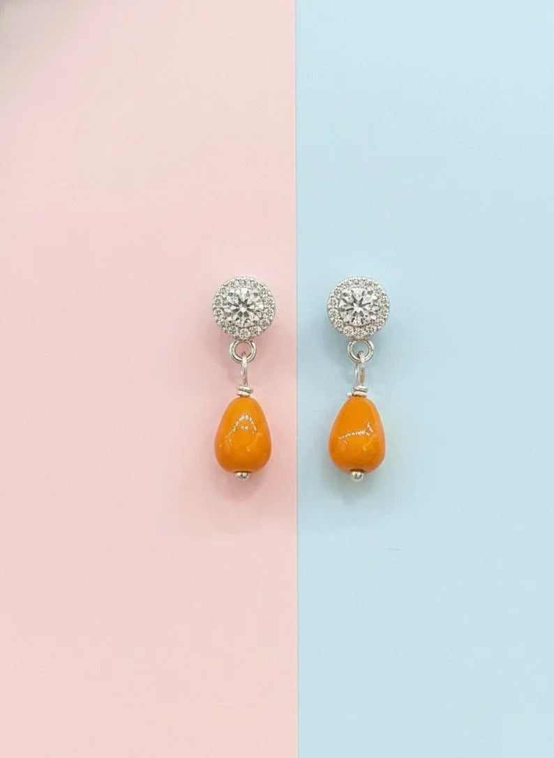 Pair of earrings with orange beads and silver tops on a pink and blue background