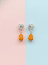 Pair of earrings with orange beads and silver tops on a pink and blue background