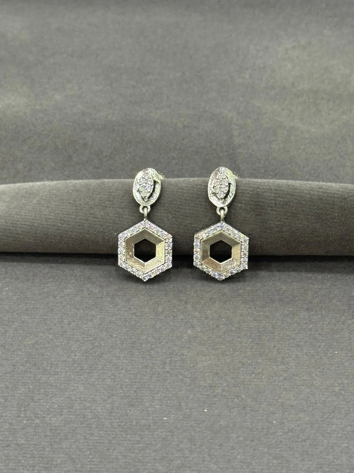 Hexagonal earrings with diamond-like stones on a gray surface