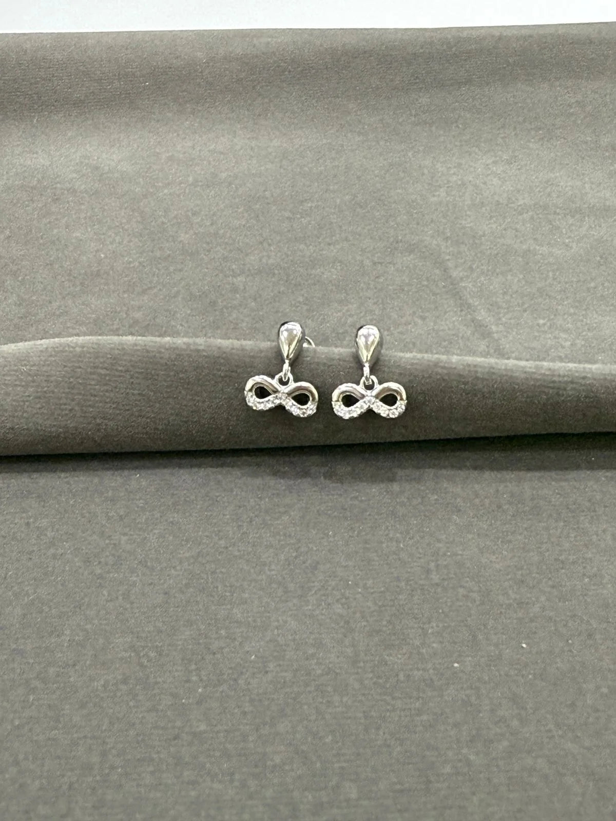 Silver infinity symbol earrings on a gray surface