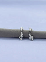 Silver music earrings on a gray surface with a light blue background