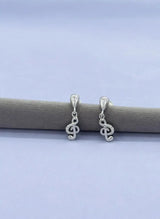 Silver treble clef earrings on a gray stick against a light blue background