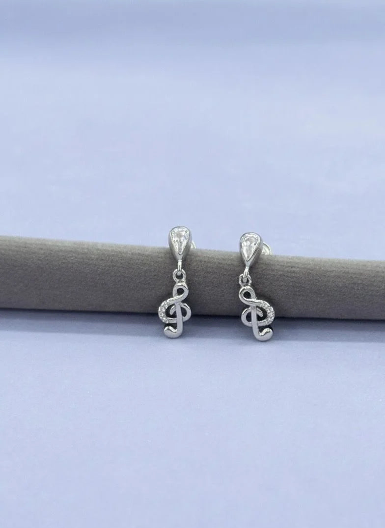 Silver treble clef earrings on a gray stick against a light blue background