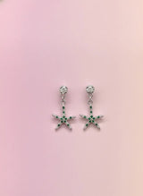Starfish-shaped earrings with green gemstones on a pink background