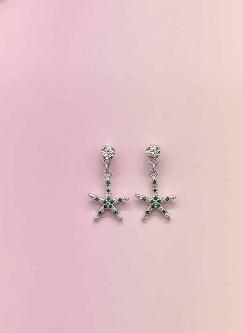 Starfish-shaped earrings with green gemstones on a pink background