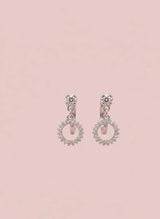 Pair of silver earrings with pink gemstones on a light pink background