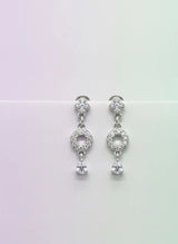 Pair of silver earrings with clear stones on a gradient background