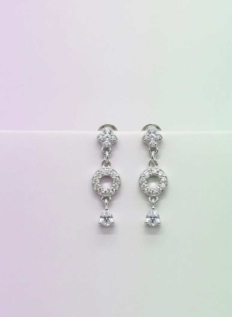 Pair of silver earrings with clear stones on a gradient background