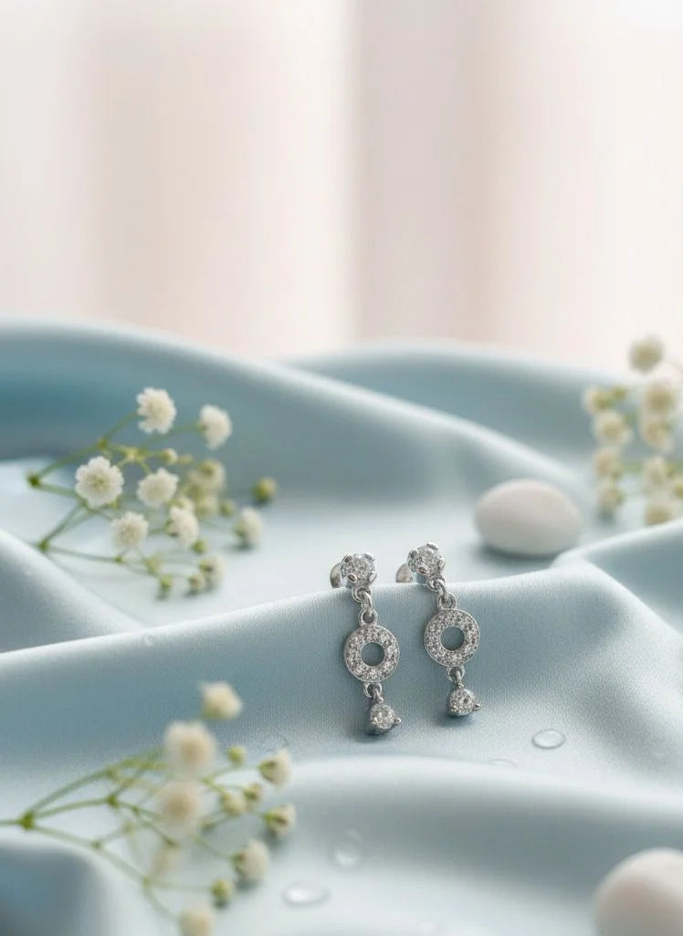 Silver earrings on a light blue fabric background with small white flowers