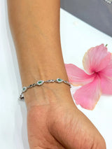Silver bracelet with green gemstones on a wrist, pink flower in the background