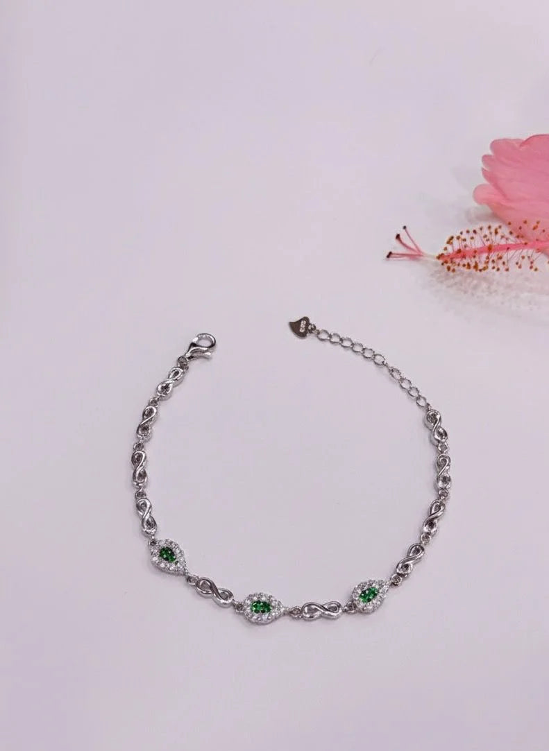 Silver bracelet with green gemstones on a light pink background