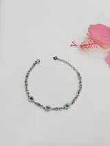 Silver bracelet with green gemstones on a light gray background with a pink flower.