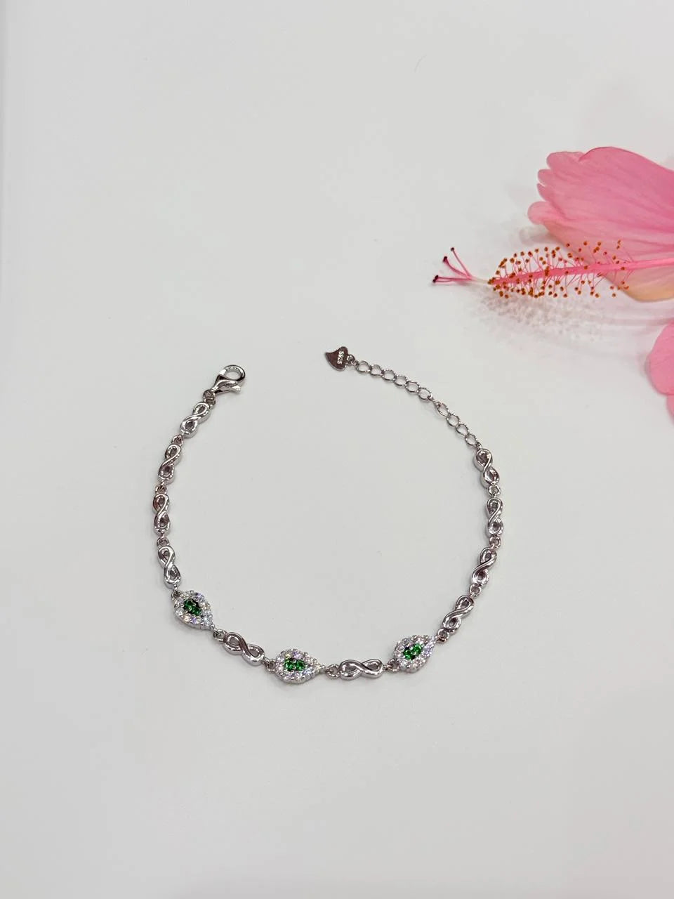 Silver bracelet with green gemstones on a light gray background with a pink flower.