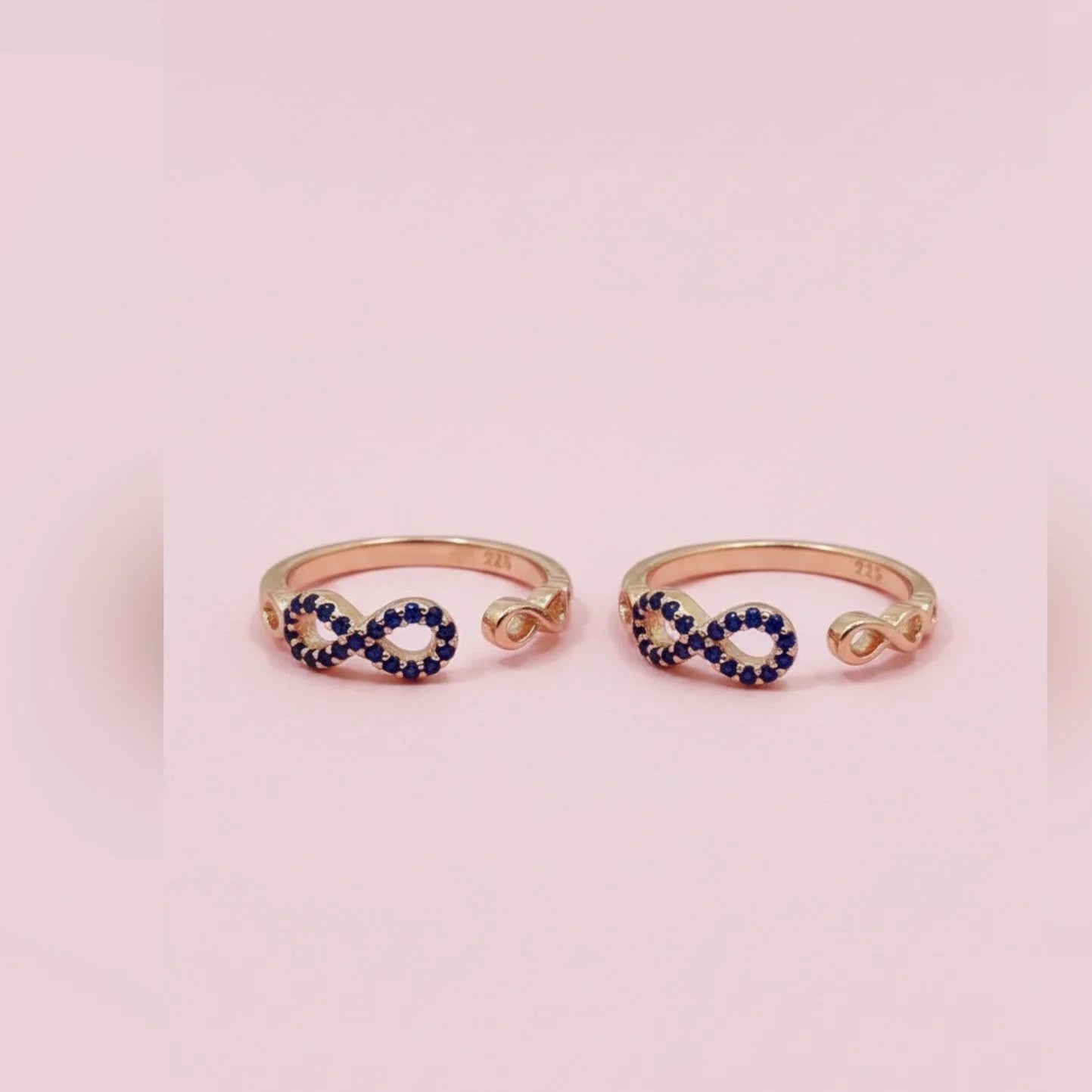 Two gold toe rings with blue gemstones on a pink background