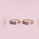 Two gold toe rings with blue gemstones on a pink background