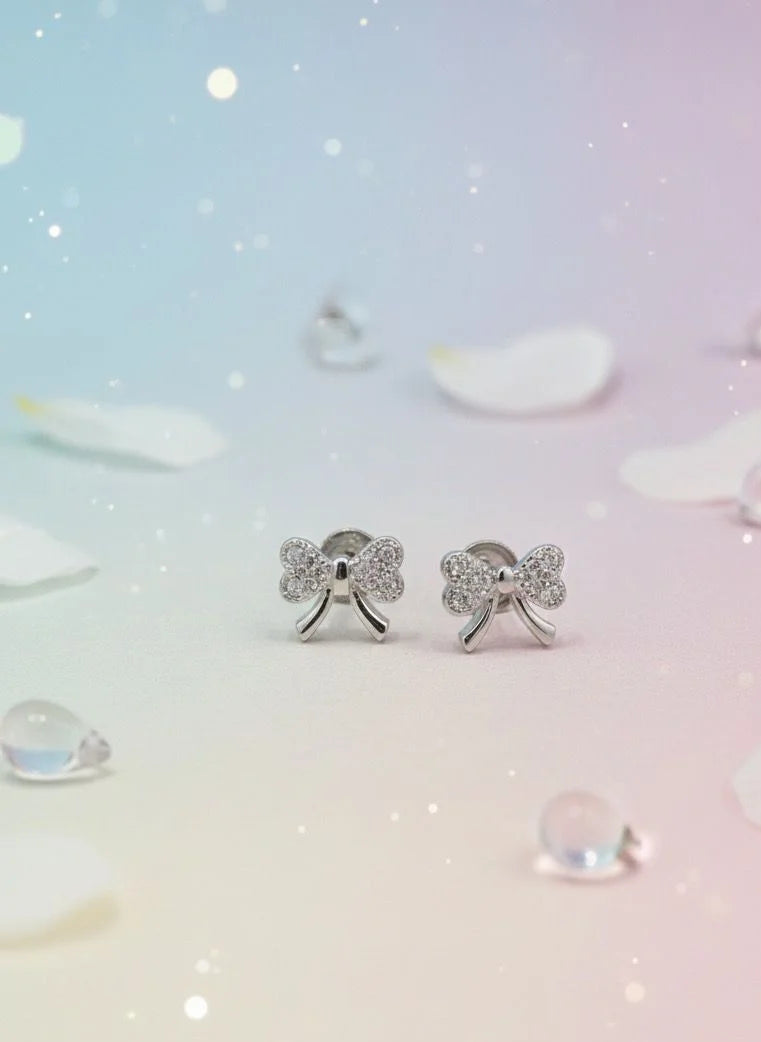 Silver bow-shaped earrings on a soft, gradient background with water droplets.