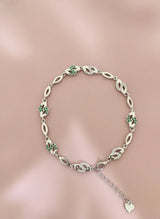 Silver bracelet with green gemstones on a pink background